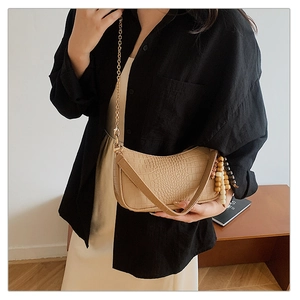 Detail of beige crocodile embossed crescent bag with gold chain and wooden bead charm