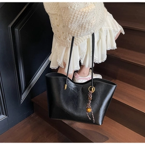 Close-up of black leather tote bag featuring a woven pendant and golden hardware details