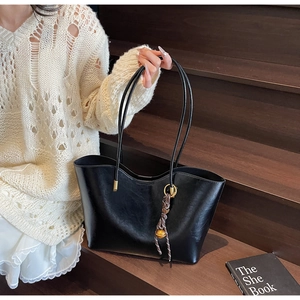 Detail of black faux leather tote bag with woven charm and slender straps