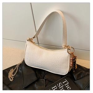 Close-up of white crocodile pattern baguette bag with wood bead tassel on leather jacket