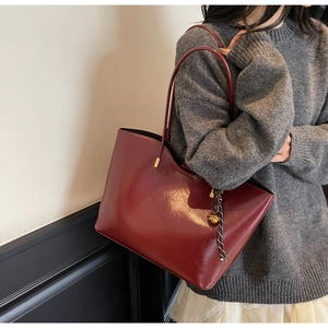 Close-up of a burgundy tote bag featuring glossy patent leather and a gold bell charm