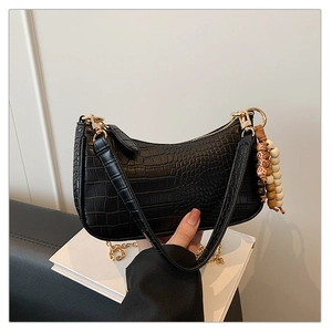 Detail of black crocodile texture baguette bag with gold chain and beaded ornament