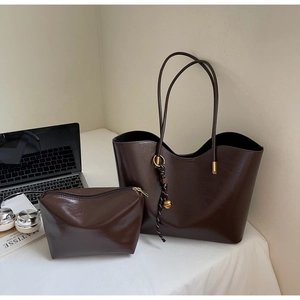 Deep brown tote bag and zipper pouch set next to a laptop and art books on desk
