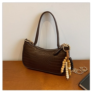 Detail of dark brown crocodile textured shoulder bag with wooden bead charm and gold chain