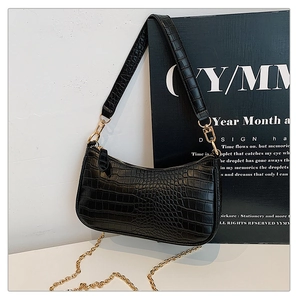 Detail of black crocodile texture baguette bag with golden chain and sleek leather strap