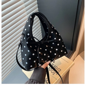 Détail du sac à pois avec nœud décoratif et bandoulière amovible posé sur des livres