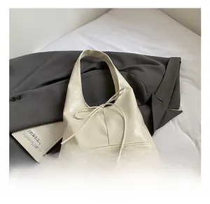 Detail showing creamy white glossy leather bag with bow on grey blazer and fabric