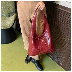 Detailed close-up of glossy burgundy tote bag featuring a decorative bow and shiny texture