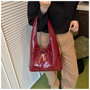 Detail of red glossy shoulder bag featuring a decorative bow knot and sleek patent finish