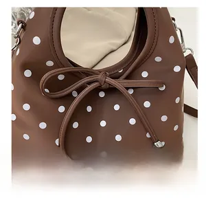 Vue détaillée du sac en cuir marron à pois avec nœud décoratif et pendentif argenté