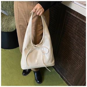 Chic cream-colored bow shoulder bag held by a model in a vintage interior setting