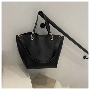 Détail d'un sac cabas en cuir noir mat avec anneaux dorés sur un fond minimaliste chic