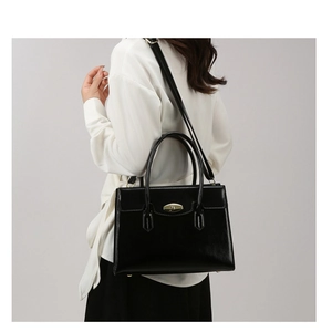 Detail of black glossy leather tote with gold twist lock and adjustable shoulder strap
