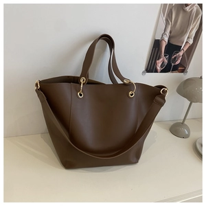 Détail du sac cabas en cuir marron foncé avec anneaux dorés sur une table minimaliste
