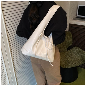 Chic beige patent leather bucket bag with bow detail worn by model in casual office setting