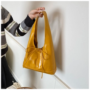 Detail of glossy ginger yellow tote bag featuring a decorative bow and smooth leather finish