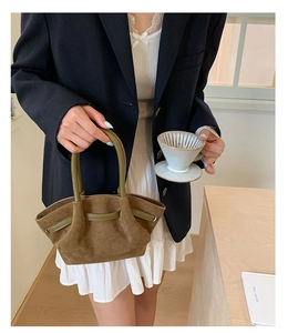 Detail of a brown suede pleated handbag with olive green handle held by a model