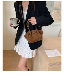 Brown suede bucket bag with pleated design and adjustable strap in lifestyle setting