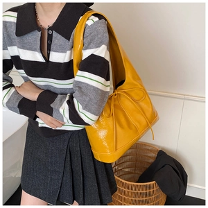 Detail of yellow glossy leather shoulder bag featuring side bow drawstring accents