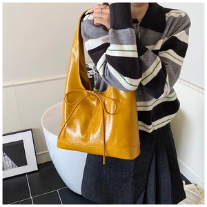 Detail of glossy yellow patent leather handbag with a stylish bow drawstring design