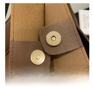 Gros plan sur les boucles magnétiques dorées à losanges d'un sac seau en daim marron