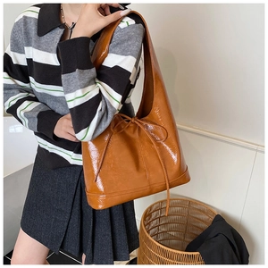 Brown patent leather shoulder bag with bow detail shown on a model in a casual setting