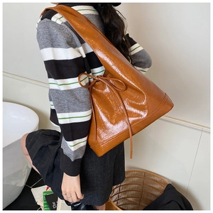 Detail of a brown glossy leather bucket bag featuring a decorative drawstring bow and wide strap