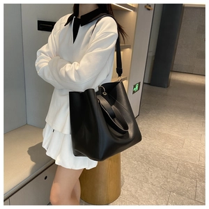 Sac seau minimaliste en cuir noir porté à l'épaule par un mannequin dans un décor moderne