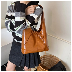 Detail of a brown glossy hobo bag with bow decoration worn as an underarm shoulder bag