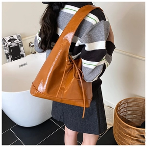 Close-up of caramel glossy patent leather shoulder bag with drawstring detail on a model