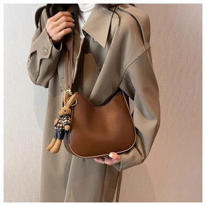 Detail of dark brown leather crescent bag with a decorative knitted bunny doll charm