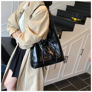 Detail of a black patent leather tote bag with a drawstring bow and glossy finish