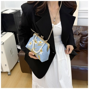 Detailed view of light blue embroidered handbag featuring white lily patterns and pearl handle