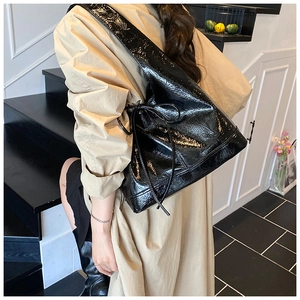 Model wearing a large black glossy shoulder bag with bow detail and crinkle texture