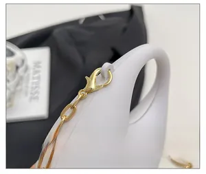 Dettaglio della catena dorata e della chiusura a moschettone su borsa in acrilico bianco