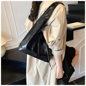 Detail of a black glossy pleated leather shoulder bag with textured finish in high-end style