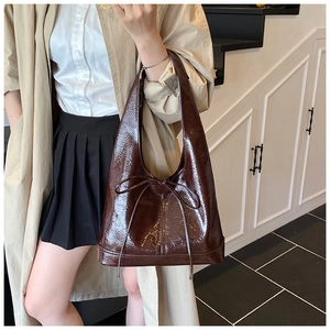 Detail of dark brown glossy leather hobo bag featuring a delicate leather bow decoration