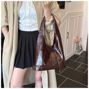 Detail of dark brown patent leather tote bag with bow accent worn on model's shoulder
