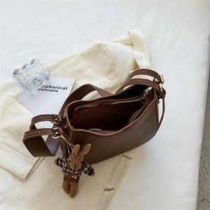 Detail of a brown leather saddle bag with a cute plush rabbit charm on a blazer