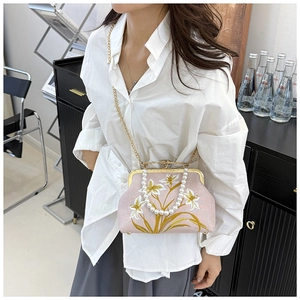 Detail of pink embroidered handbag featuring pearl handle and gold chain strap