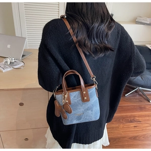 Detail der blauen Denim-Beuteltasche mit braunem Lederbesatz und Bärenanhänger