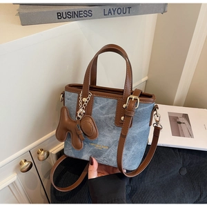 Detail der blauen Denim Beuteltasche mit braunen Ledergriffen und goldenem Hundeanhänger