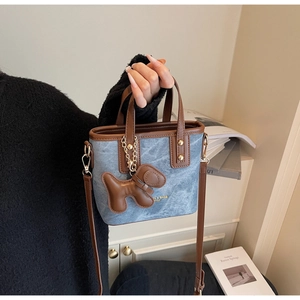Detail einer Vintage-Denim-Umhängetasche mit Kontrast-Lederbesatz und Hundeanhänger
