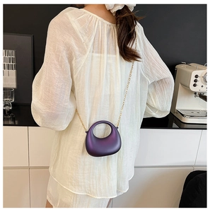 Dettaglio di una mini borsa a mezzaluna viola con catena dorata indossata da una modella