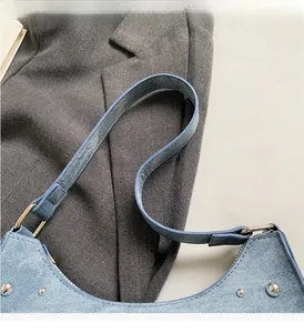 Détail du sac en denim bleu clair avec rivets argentés et boucles métalliques