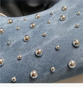 Détail d'un sac à main en denim bleu clair avec des rivets argentés et texture sergé