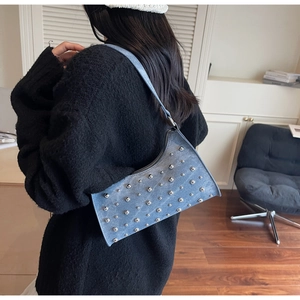 Gros plan d'un sac sous les bras en denim bleu à clous argentés porté sur un pull noir