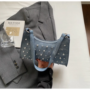 Détail du sac à épaule en jean bleu avec clous argentés sur fond de blazer gris élégant