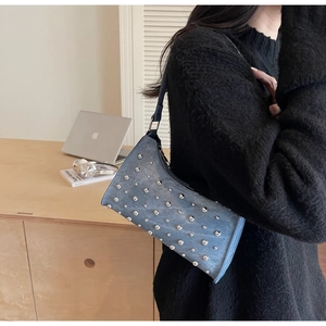 Détail du sac à bandoulière en denim bleu avec rivets argentés et bandoulière en cuir
