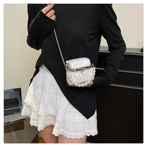 Detail of white quilted handbag featuring pearl handle and elegant metallic chain strap